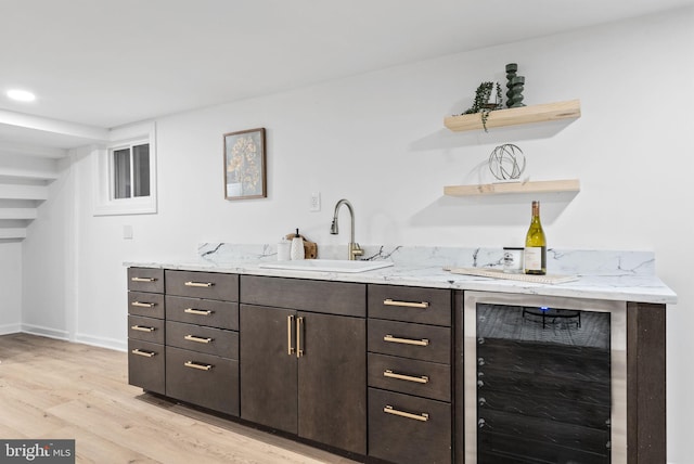 bar featuring light hardwood / wood-style flooring, sink, light stone counters, dark brown cabinetry, and wine cooler