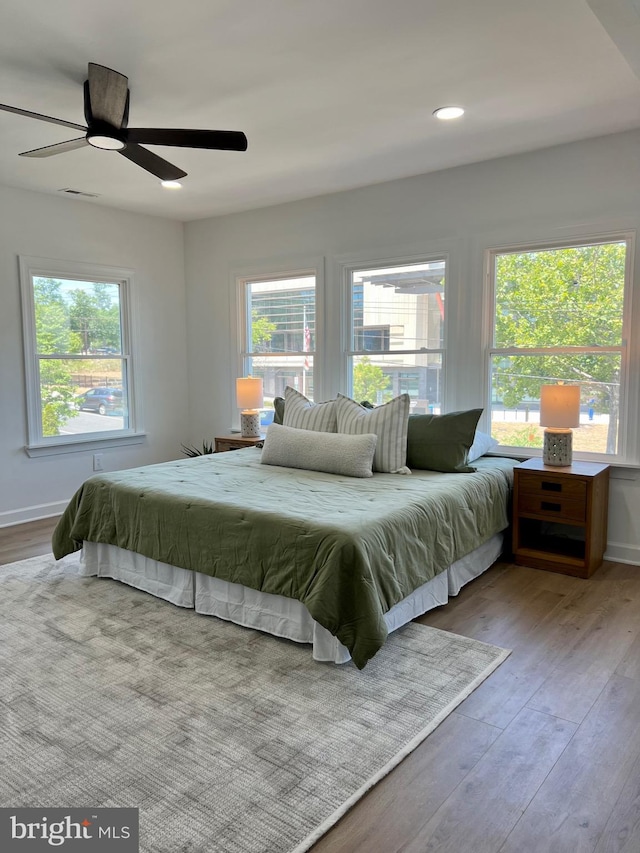 bedroom with multiple windows, wood-type flooring, and ceiling fan