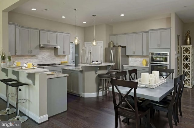 kitchen featuring decorative light fixtures, gray cabinets, light stone countertops, a kitchen breakfast bar, and stainless steel appliances