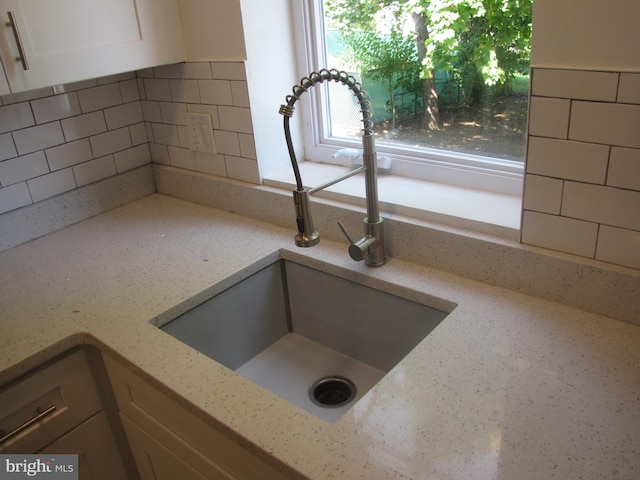 details with white cabinetry, light stone countertops, sink, and tasteful backsplash