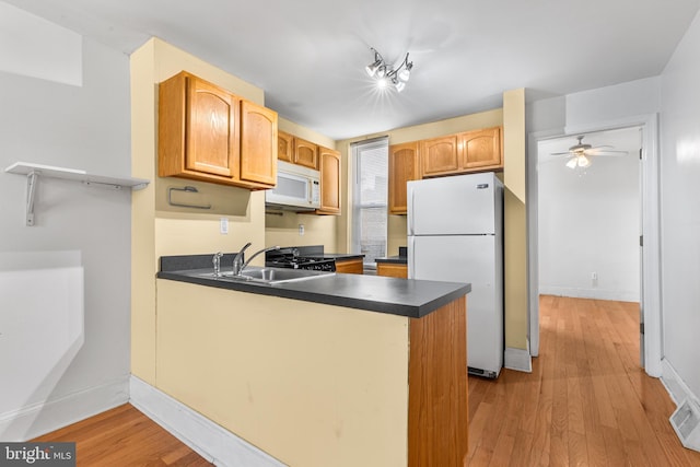 kitchen featuring ceiling fan, kitchen peninsula, sink, white appliances, and light wood-type flooring