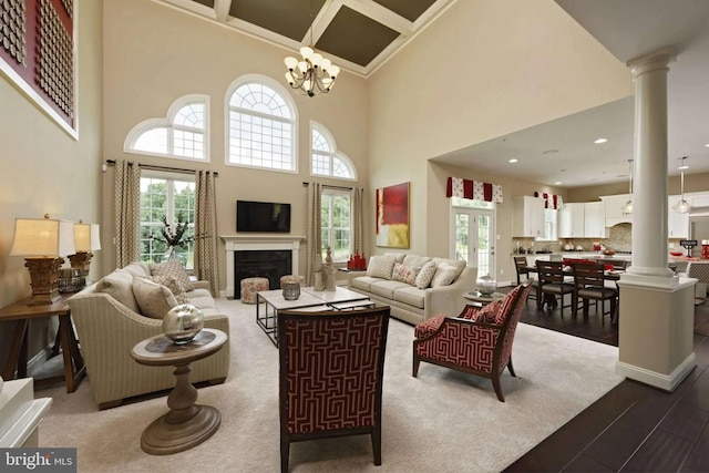 living room featuring hardwood / wood-style floors, ornate columns, a towering ceiling, and an inviting chandelier