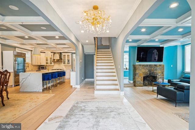 foyer entrance with a fireplace, light hardwood / wood-style floors, beamed ceiling, an inviting chandelier, and coffered ceiling