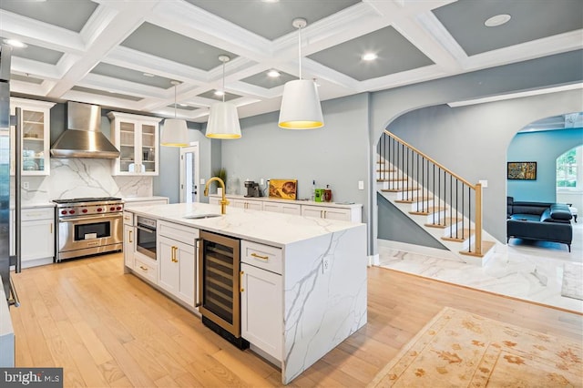 kitchen featuring backsplash, wall chimney range hood, designer range, sink, and beverage cooler