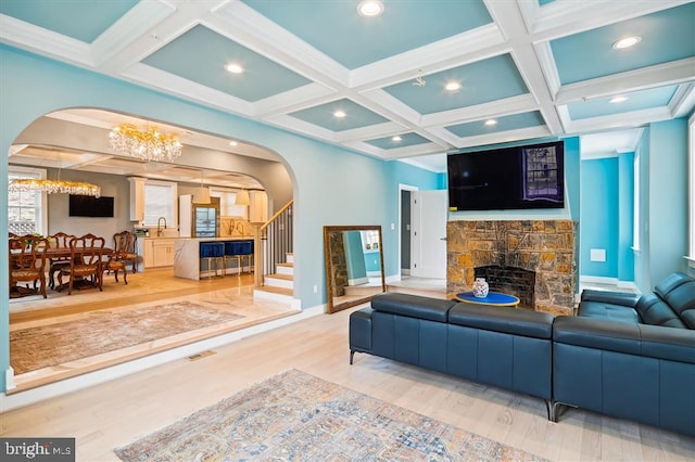 living room featuring a fireplace, beam ceiling, an inviting chandelier, coffered ceiling, and hardwood / wood-style flooring