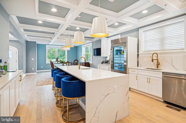 kitchen with appliances with stainless steel finishes, decorative light fixtures, an island with sink, sink, and light stone counters