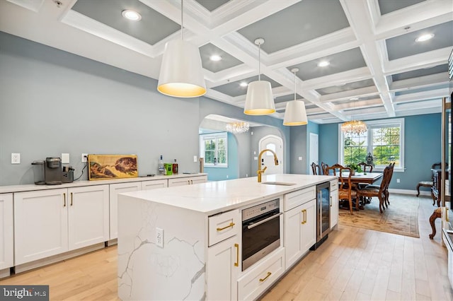 kitchen featuring decorative light fixtures, sink, a kitchen island with sink, white cabinets, and a chandelier