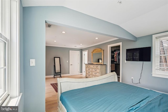 bedroom with vaulted ceiling, light hardwood / wood-style floors, crown molding, a walk in closet, and a closet