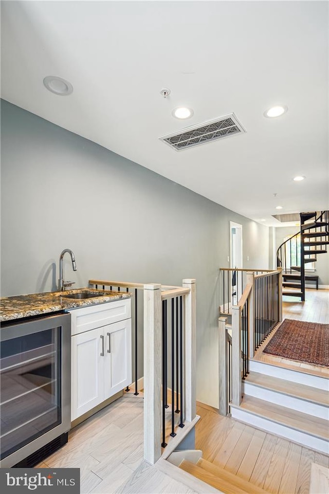 bar with wine cooler, dark stone countertops, light hardwood / wood-style floors, sink, and white cabinetry