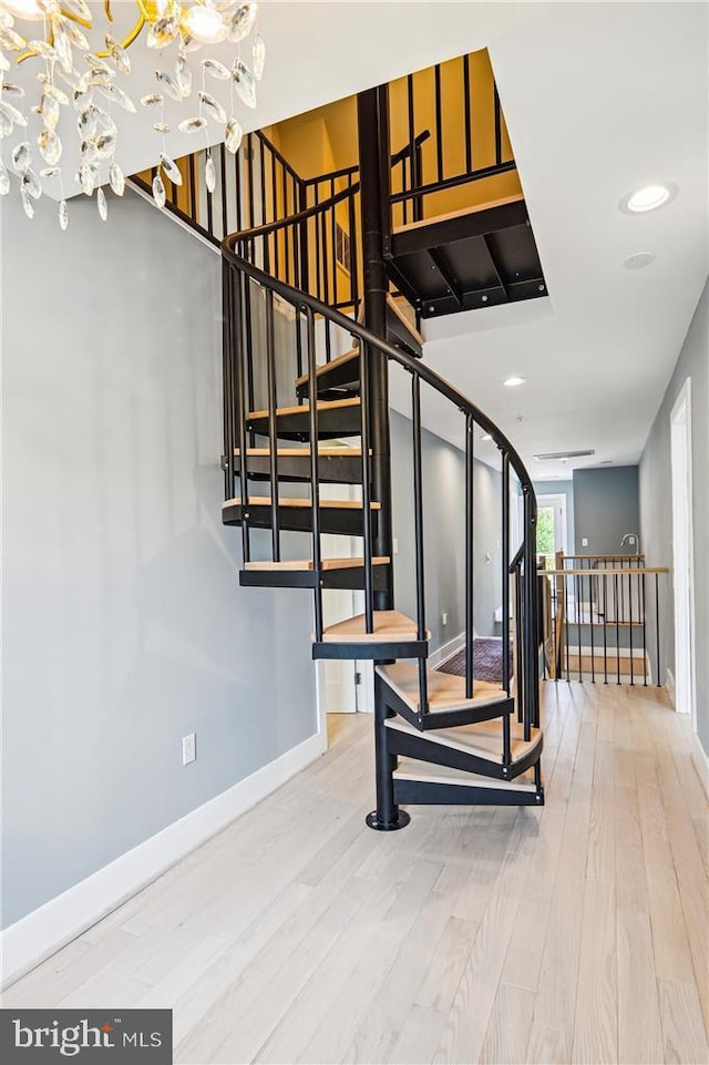 staircase with wood-type flooring and an inviting chandelier