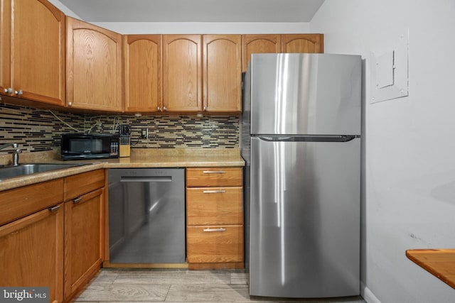 kitchen with tasteful backsplash, appliances with stainless steel finishes, sink, and light hardwood / wood-style flooring