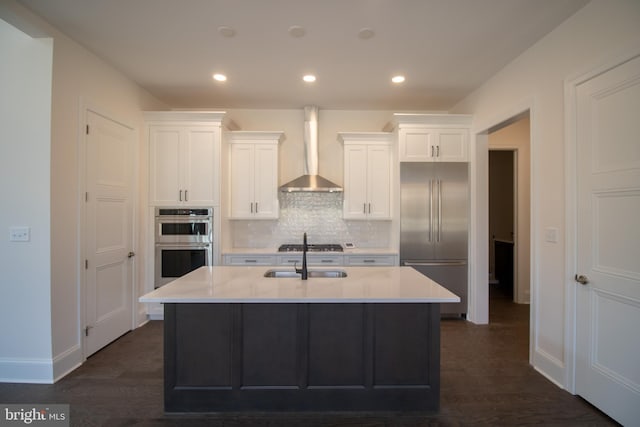 kitchen featuring white cabinets, appliances with stainless steel finishes, a kitchen island with sink, and wall chimney range hood