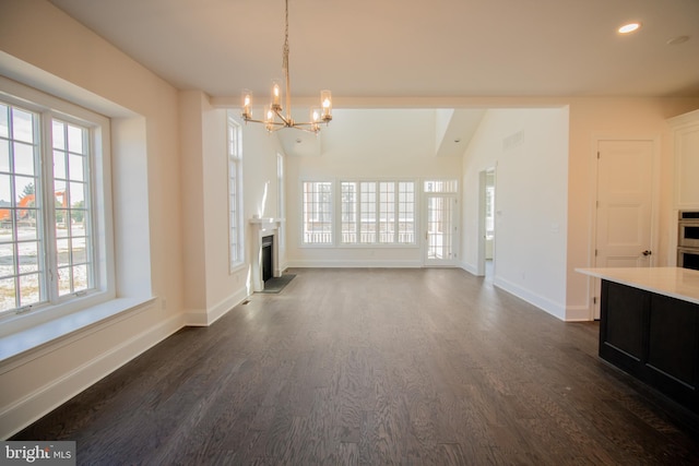 unfurnished living room with a wealth of natural light, dark wood-type flooring, and a chandelier