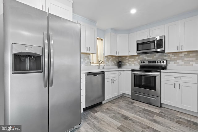 kitchen with tasteful backsplash, white cabinets, light hardwood / wood-style floors, appliances with stainless steel finishes, and sink