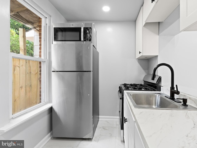 kitchen with stainless steel appliances, white cabinetry, light stone counters, and sink