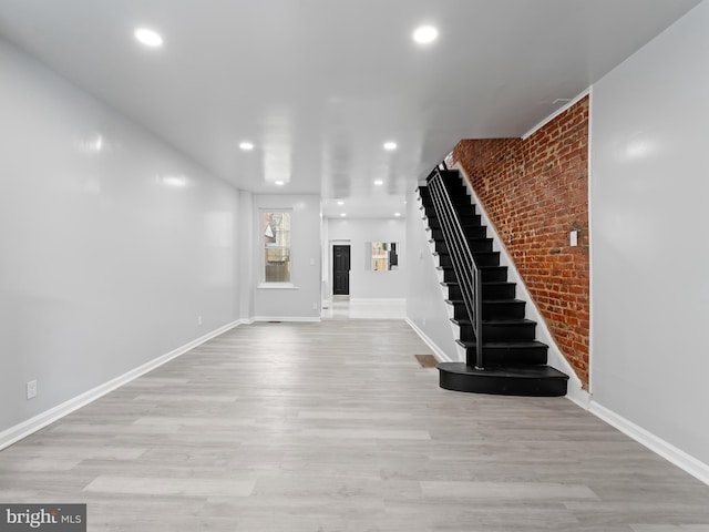 unfurnished living room featuring brick wall and light wood-type flooring