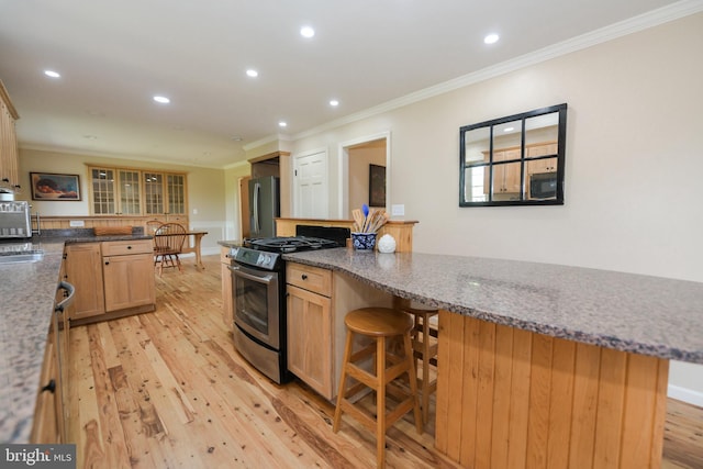 kitchen featuring a kitchen bar, stainless steel appliances, dark stone countertops, ornamental molding, and light hardwood / wood-style flooring