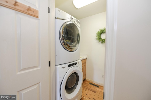 clothes washing area with light wood-type flooring, stacked washer and dryer, and cabinets