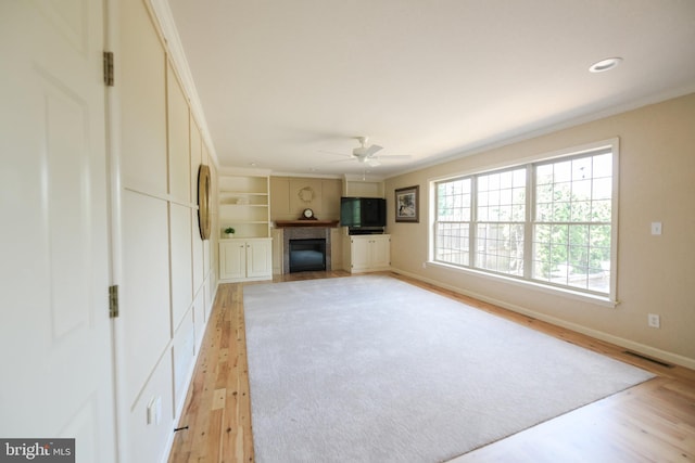 unfurnished living room with ceiling fan, built in shelves, light hardwood / wood-style flooring, and crown molding