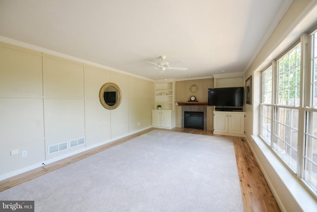 unfurnished living room featuring ceiling fan, built in features, ornamental molding, and light hardwood / wood-style flooring