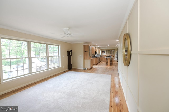 unfurnished living room featuring ceiling fan, ornamental molding, and light wood-type flooring