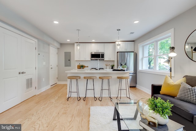 kitchen with a breakfast bar, light wood-type flooring, electric panel, stainless steel appliances, and hanging light fixtures