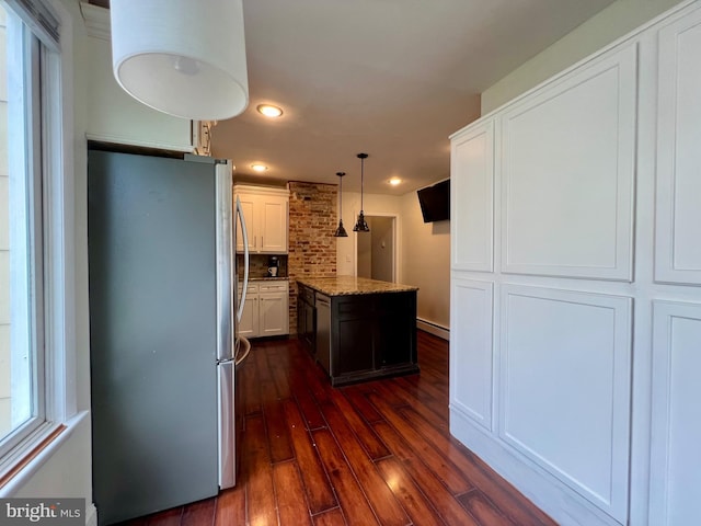 kitchen featuring light stone countertops, tasteful backsplash, a kitchen island, white cabinets, and stainless steel refrigerator