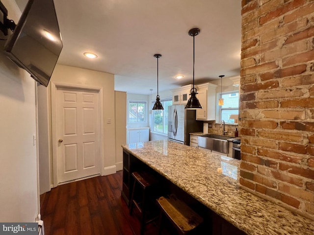 kitchen with white cabinets, hanging light fixtures, light stone countertops, dark hardwood / wood-style flooring, and stainless steel fridge with ice dispenser