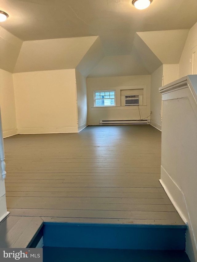 additional living space with a wall mounted air conditioner, baseboard heating, hardwood / wood-style flooring, and vaulted ceiling