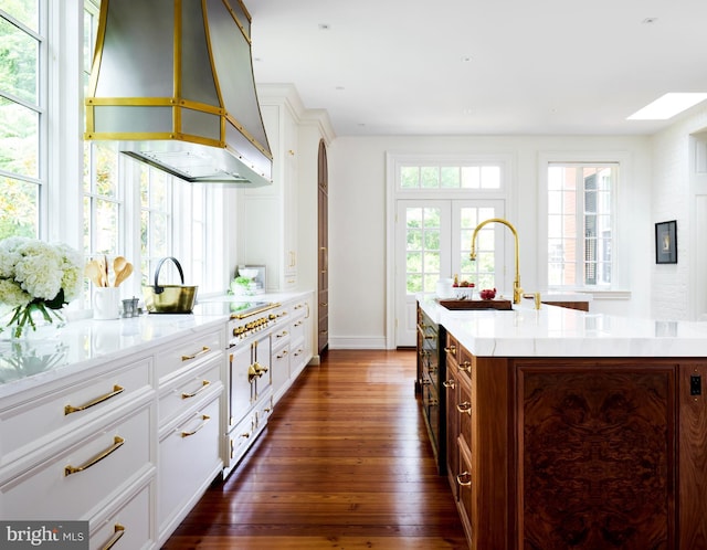 kitchen featuring dark hardwood / wood-style flooring, ventilation hood, sink, a center island with sink, and white cabinetry