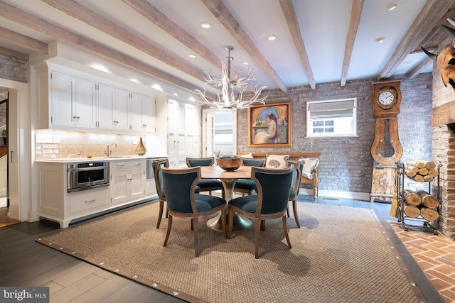 dining space featuring sink, hardwood / wood-style flooring, beamed ceiling, brick wall, and a chandelier