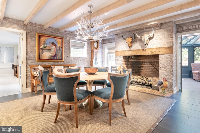 dining space with hardwood / wood-style floors, a notable chandelier, beamed ceiling, and a brick fireplace