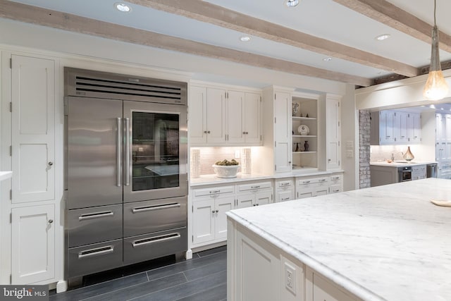 kitchen with pendant lighting, built in fridge, white cabinets, beam ceiling, and light stone counters