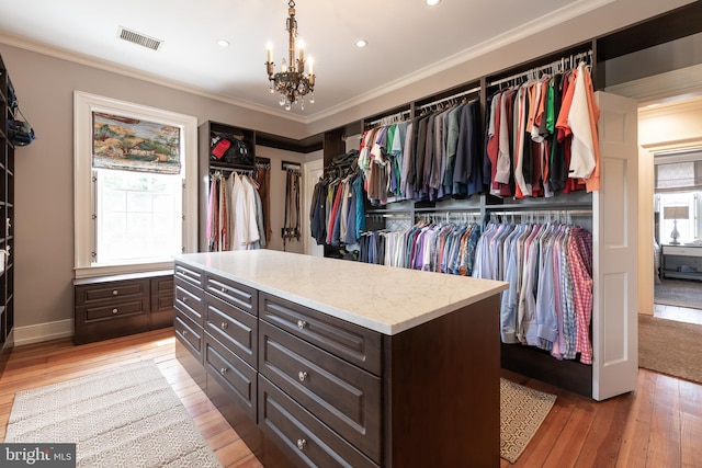 spacious closet with light hardwood / wood-style floors and a notable chandelier