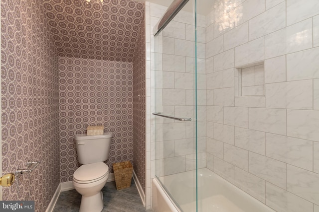 bathroom featuring toilet and shower / bath combination with glass door