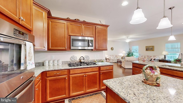 kitchen featuring light stone counters, sink, stainless steel appliances, and decorative light fixtures