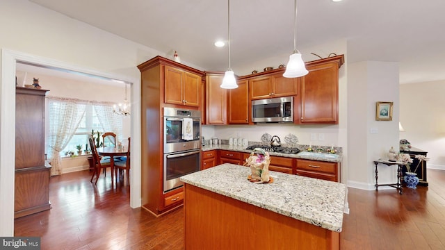 kitchen featuring light stone counters, stainless steel appliances, dark wood-type flooring, pendant lighting, and a center island