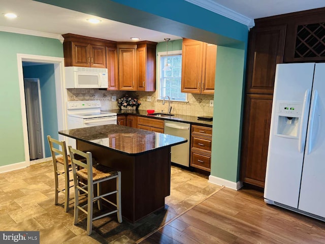 kitchen with a breakfast bar, white appliances, sink, hanging light fixtures, and a kitchen island