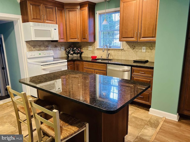 kitchen with a kitchen bar, dark stone counters, white appliances, sink, and pendant lighting