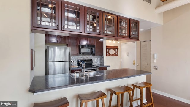 kitchen featuring dark wood-type flooring, black appliances, a kitchen breakfast bar, sink, and decorative backsplash