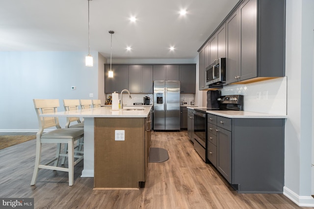 kitchen with a center island with sink, stainless steel appliances, decorative backsplash, a kitchen breakfast bar, and hanging light fixtures