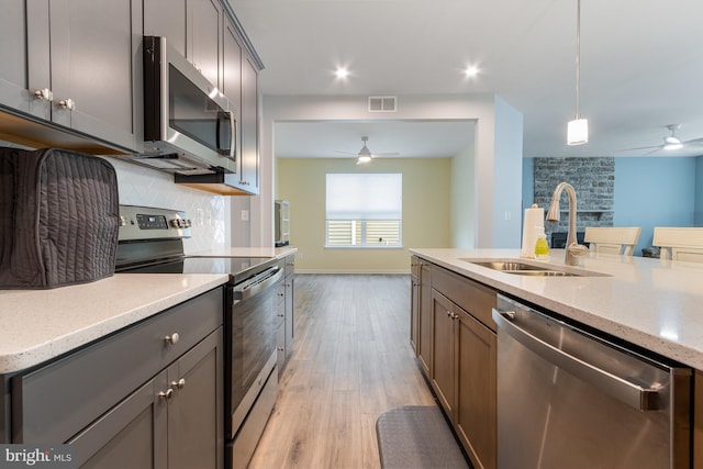 kitchen with light hardwood / wood-style floors, appliances with stainless steel finishes, hanging light fixtures, light stone countertops, and sink