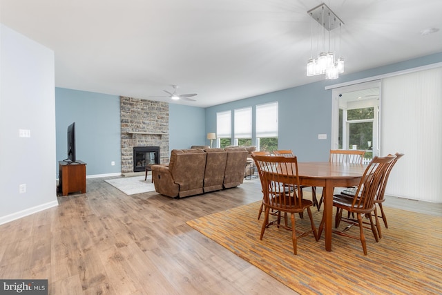 dining space featuring a fireplace, ceiling fan with notable chandelier, and light hardwood / wood-style floors