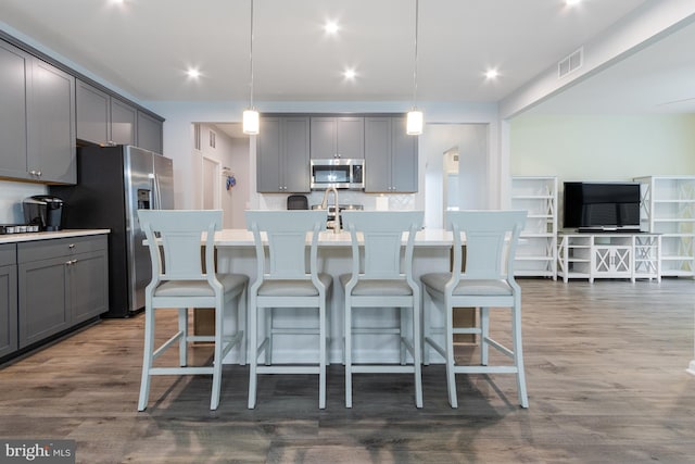 kitchen with a center island with sink, stainless steel appliances, backsplash, and hanging light fixtures