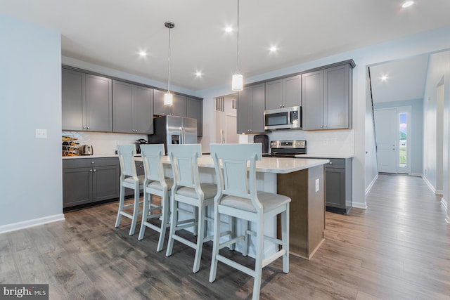 kitchen featuring dark hardwood / wood-style floors, pendant lighting, a kitchen island with sink, gray cabinetry, and stainless steel appliances