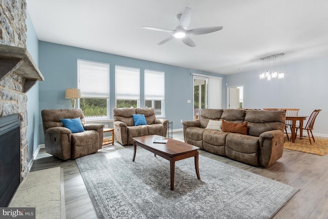 living room featuring a fireplace, ceiling fan with notable chandelier, and light hardwood / wood-style flooring