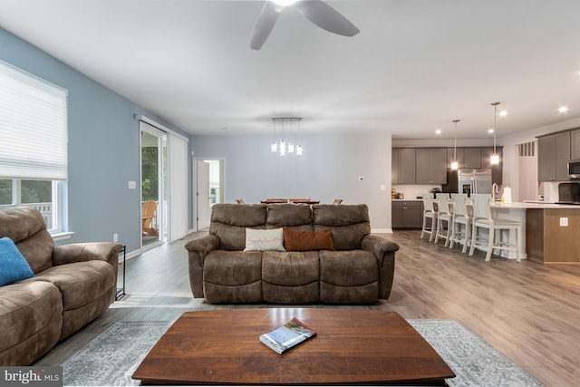 living room with ceiling fan with notable chandelier and light hardwood / wood-style flooring