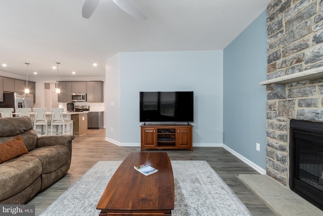 living room with ceiling fan, dark hardwood / wood-style floors, and a stone fireplace