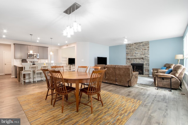 dining area featuring light wood-type flooring, a fireplace, and ceiling fan with notable chandelier