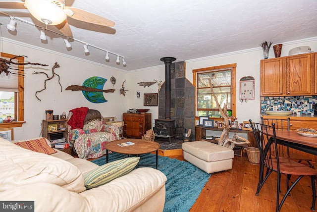 living room featuring a textured ceiling, ceiling fan, crown molding, light hardwood / wood-style flooring, and a wood stove